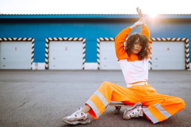 Gün batımında sokakta dans eden genç, sportif kadın dansçı. Turuncu takım elbiseli Afro-Amerikalı kadın bazı hareketler gösteriyor. Spor, dans ve şehir kültürü konsepti.