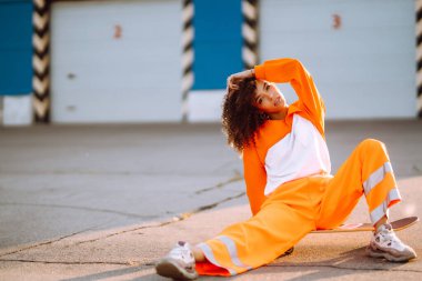 Gün batımında sokakta dans eden genç, sportif kadın dansçı. Turuncu takım elbiseli Afro-Amerikalı kadın bazı hareketler gösteriyor. Spor, dans ve şehir kültürü konsepti.