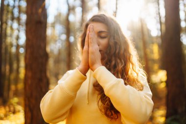 Yoga yapan rahat bir kadın, güneşli sonbahar ormanlarında kollarını açıyor. Renkli yapraklarla çevrili havanın tadını çıkaran ve nefes egzersizleri yapan genç bir kadın. Rahatlama, dinlenme konsepti.