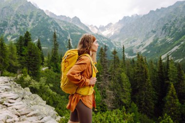 Güneşli bir günde, kayalık bir yolda sarı sırt çantalı bir bayan yürüyüşçü. Mutlu kadın dağ manzarasının tadını çıkarıyor ve açık havada özgürlüğü hissediyor. Doğa, macera konsepti.