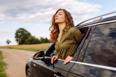 Kıvırcık saçlı, gülümseyen kadın arabanın camından dışarı bakıyor. Genç gezgin araba yolculuğundan zevk alır ve araba penceresinden özgürlüğü hisseder. Macera, özgürlük kavramı.