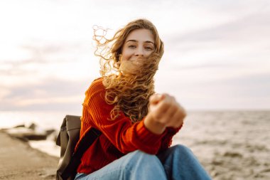 Mutlu kadın iskelede deniz feneriyle eğleniyor. Sırt çantalı bir turist gün batımında deniz manzarasının tadını çıkarıyor ve denizin özgürlüğünü hissediyor. Doğa ve eğlence kavramı.