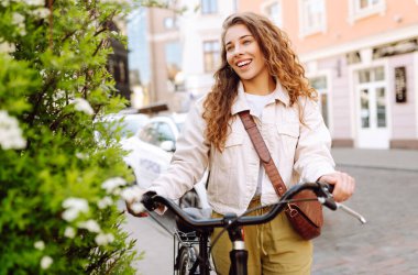 Güneşli bir caddede bisikletli neşeli genç bir kadın duruyor. Güzel bir kadın gün batımını sever, bisiklet sürer. Turizm, eğlence konsepti. Yaşam biçimi.