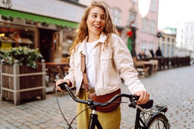 Güneşli bir caddede bisikletli neşeli genç bir kadın duruyor. Güzel bir kadın gün batımını sever, bisiklet sürer. Turizm, eğlence konsepti. Yaşam biçimi.