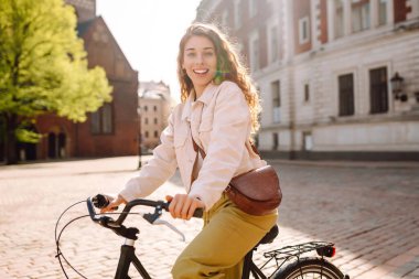 Güneşli bir caddede bisikletli neşeli genç bir kadın duruyor. Güzel bir kadın gün batımını sever, bisiklet sürer. Turizm, eğlence konsepti. Yaşam biçimi.