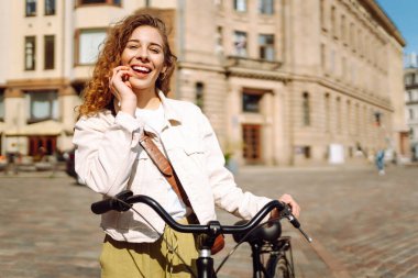Güneşli bir caddede bisikletli neşeli genç bir kadın duruyor. Güzel bir kadın gün batımını sever, bisiklet sürer. Turizm, eğlence konsepti. Yaşam biçimi.