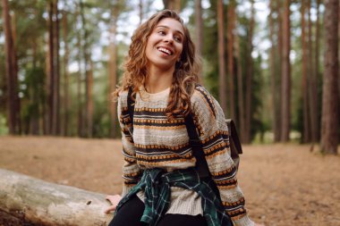 Sırt çantalı güzel bir kadın ormanda doğanın tadını çıkarıyor. Yolculukta olan genç bir kadın, açık havada bir kütükte dinleniyor. Boş zaman konsepti, macera. Yaşam biçimi.