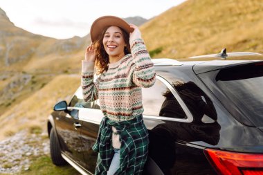 Şapkalı neşeli bir kadın bir arabanın bagajında oturur ve dağ manzarasına hayran kalır. Araba gezisinde olan bir kadın günbatımının ve dağların tadını çıkarır. Ulaşım konsepti, macera.