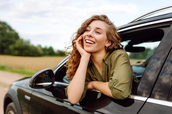 Kıvırcık saçlı, gülümseyen kadın arabanın camından dışarı bakıyor. Genç gezgin araba yolculuğundan zevk alır ve araba penceresinden özgürlüğü hisseder. Macera, özgürlük kavramı.