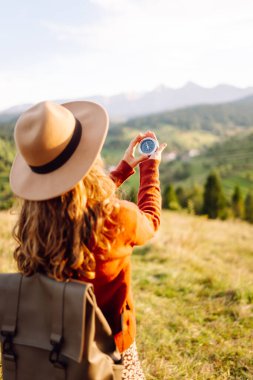 Güneşli bir günde sırt çantası ve pusula tutan kadın yürüyüşçünün arka görüntüsü. Yürüyüş yolu arayan kadın yürüyüşçü, gün batımının tadını çıkarıyor. Navigasyon kavramı.