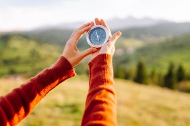 Güneşli bir günde sırt çantası ve pusula tutan kadın yürüyüşçünün arka görüntüsü. Yürüyüş yolu arayan kadın yürüyüşçü, gün batımının tadını çıkarıyor. Navigasyon kavramı.