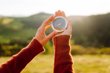 Güneşli bir günde sırt çantası ve pusula tutan kadın yürüyüşçünün arka görüntüsü. Yürüyüş yolu arayan kadın yürüyüşçü, gün batımının tadını çıkarıyor. Navigasyon kavramı.