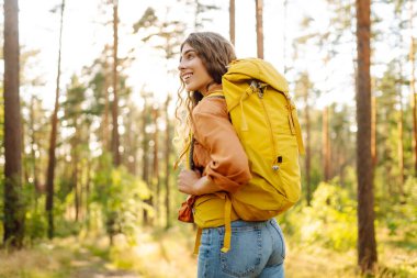 Parlak bir sırt çantası olan mutlu bir yürüyüşçü güneş ışınlarında bir ağacın altında oturur. Güzel bir kadın sonbahar ormanında bir maceranın tadını çıkarır. Kavram: yürüyüş, rahatlama, doğa. Etkin yaşam biçimi.