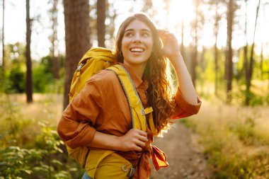 Parlak bir sırt çantası olan mutlu bir yürüyüşçü güneş ışınlarında bir ağacın altında oturur. Güzel bir kadın sonbahar ormanında bir maceranın tadını çıkarır. Kavram: yürüyüş, rahatlama, doğa. Etkin yaşam biçimi.