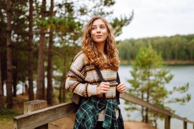 Sırt çantalı bir kadın, göle giden tahta merdivenlerde duruyor. Gezgin sonbahar ormanlarında yürüyüş yaparak doğanın tadını çıkarıyor. Macera mekanı, hafta sonu.