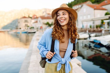 Şapka takan ve bir evrak çantası taşıyan genç bir kadının portresi. Resimli bir kasabada denizde geziniyor. Gezgin deniz manzarasının tadını çıkarıyor. Turizm ve keyif kavramı.