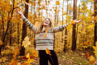 Sarı yağmurluklu genç bir kadın güneşli bir günde sonbahar ormanında gezinir. Neşeli bir sırt çantası güz mevsiminin güzelliğinin tadını çıkarır. Macera ve mevsimlik kavramı.
