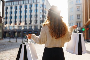 Güneşli bir günde elinde poşet tutan şapkalı gülümseyen bir kadının portresi. Genç bir kadın alışveriş yaptıktan sonra kalabalık bir şehirde dolaşır. İndirim kavramı, hafta sonu.