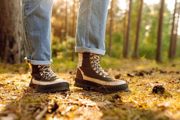 Batan güneşin ışınlarıyla orman yolunda yürüyen çizmeli bir yürüyüşçünün yakın çekimi. Ormanda yeni yerler keşfeden ve maceranın tadını çıkaran bir kadının bacakları. Yürüyüş kavramı, mevsimlik.