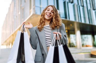 Alışveriş çantalı neşeli bir kadın modern bir alışveriş merkezinin yakınında eğleniyor. Güzel bir kadın, alışverişlerinin çantalarla yapılmasının keyfini çıkarır. Tüketim kavramı, indirimler.