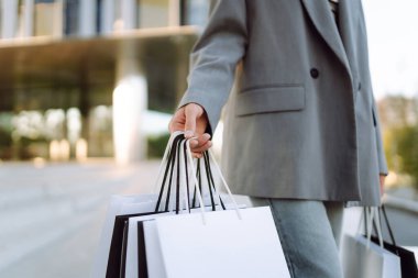 Alışveriş çantalı neşeli bir kadın modern bir alışveriş merkezinin yakınında eğleniyor. Güzel bir kadın, alışverişlerinin çantalarla yapılmasının keyfini çıkarır. Tüketim kavramı, indirimler.