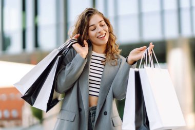 Alışveriş çantalı neşeli bir kadın modern bir alışveriş merkezinin yakınında eğleniyor. Güzel bir kadın, alışverişlerinin çantalarla yapılmasının keyfini çıkarır. Tüketim kavramı, indirimler.