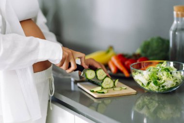 Genç hamile bir kadın modern bir mutfakta dururken kereviz doğruyor. Müstakbel güzel bir anne sıcak bir odada taze meyve ve sebze seçer. Sağlıklı yaşam tarzı, beslenme, yiyecek kavramları.