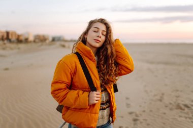 Sırt çantalı güzel bir kadın şafak vakti kıyıda geziniyor. Gezgin güneş ışınlarındaki deniz manzarasının tadını çıkarıyor. Seyahat, keyif ve özgürlük kavramları.