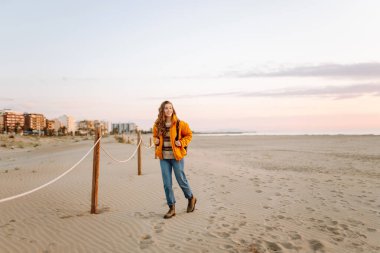 Sırt çantalı güzel bir kadın şafak vakti kıyıda geziniyor. Gezgin güneş ışınlarındaki deniz manzarasının tadını çıkarıyor. Seyahat, keyif ve özgürlük kavramları.
