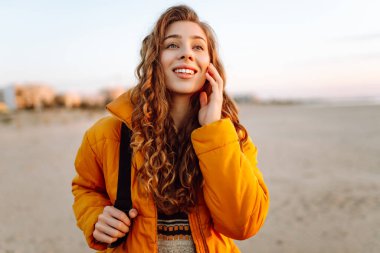 Sırt çantalı güzel bir kadın şafak vakti kıyıda geziniyor. Gezgin güneş ışınlarındaki deniz manzarasının tadını çıkarıyor. Seyahat, keyif ve özgürlük kavramları.