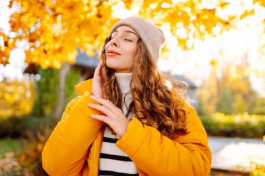 Sırt çantası ve parlak ceketli genç bir gezginin portresi sonbahar parkında gün batımında geziniyor. Mutlu kadın ormanda eğleniyor ve güneşli bir günün tadını çıkarıyor. Seyahat ve hafta sonu kavramı.