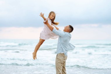 Bir baba ve küçük kızı deniz kıyısında el ele geziyorlar. Mutlu bir adam ve çocuğu dışarıda eğleniyor, birlikte eğleniyorlar. Çocukluk kavramı, rahatlama..