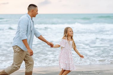 Bir baba ve küçük kızı deniz kıyısında el ele geziyorlar. Mutlu bir adam ve çocuğu dışarıda eğleniyor, birlikte eğleniyorlar. Çocukluk kavramı, rahatlama..