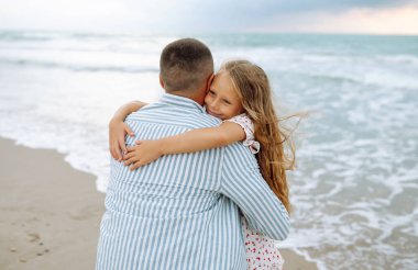 Bir baba ve küçük kızı deniz kıyısında el ele geziyorlar. Mutlu bir adam ve çocuğu dışarıda eğleniyor, birlikte eğleniyorlar. Çocukluk kavramı, rahatlama..