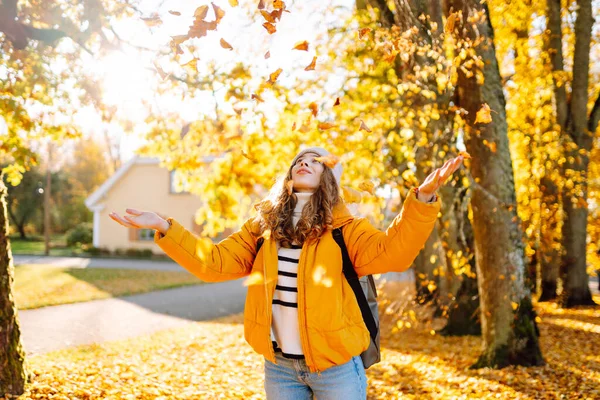 Tatlı bir kadın sonbahar parkında düşen yapraklarla eğleniyor. Güzel bir kadın günbatımında sonbahar yapraklarını havaya fırlatır. Mevsimlik, eğlence ve rahatlama kavramı.