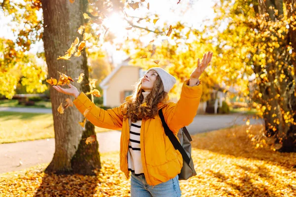 Tatlı bir kadın sonbahar parkında düşen yapraklarla eğleniyor. Güzel bir kadın günbatımında sonbahar yapraklarını havaya fırlatır. Mevsimlik, eğlence ve rahatlama kavramı.