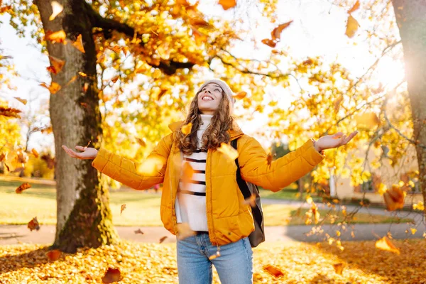 Tatlı bir kadın sonbahar parkında düşen yapraklarla eğleniyor. Güzel bir kadın günbatımında sonbahar yapraklarını havaya fırlatır. Mevsimlik, eğlence ve rahatlama kavramı.