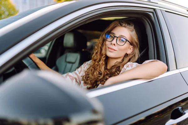 Güneşli bir günde direksiyonun başına geçip yola bakan gözlüklü genç bir kadının portresi. Güzel bir kadın sürücü araba sürmekten hoşlanır. Ulaşım ve eğlence kavramı.