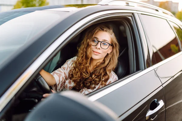 Güneşli bir günde direksiyonun başına geçip yola bakan gözlüklü genç bir kadının portresi. Güzel bir kadın sürücü araba sürmekten hoşlanır. Ulaşım ve eğlence kavramı.