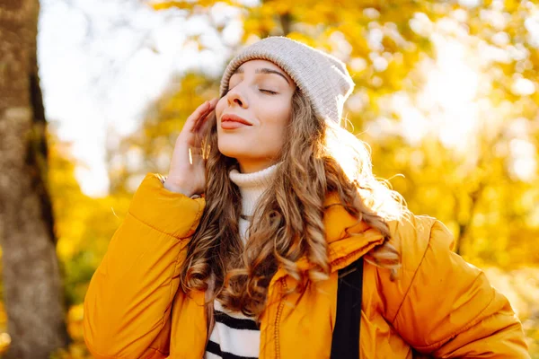 Sırt çantası ve parlak ceketli genç bir gezginin portresi sonbahar parkında gün batımında geziniyor. Mutlu kadın ormanda eğleniyor ve güneşli bir günün tadını çıkarıyor. Seyahat ve hafta sonu kavramı.