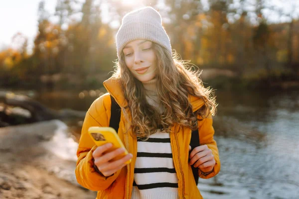 Parlak sarı ceketli tatlı bir kadın, nehrin kenarındaki güneşli bir ormanda telefonuyla konuşuyor. Güzel bir gezgin mesajlaşır ve gün batımını seyreder. Macera ve blog konsepti.