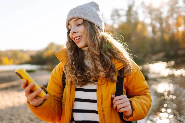 Parlak sarı ceketli tatlı bir kadın, nehrin kenarındaki güneşli bir ormanda telefonuyla konuşuyor. Güzel bir gezgin mesajlaşır ve gün batımını seyreder. Macera ve blog konsepti.