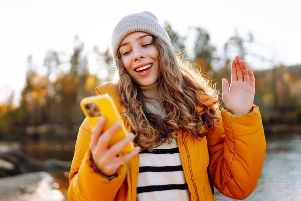 Parlak sarı ceketli tatlı bir kadın, nehrin kenarındaki güneşli bir ormanda telefonuyla konuşuyor. Güzel bir gezgin mesajlaşır ve gün batımını seyreder. Macera ve blog konsepti.