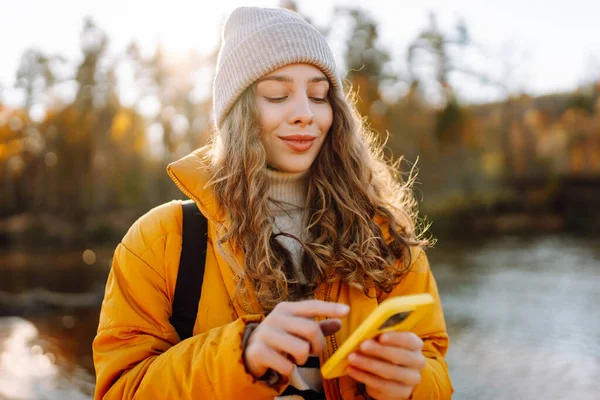 Parlak sarı ceketli tatlı bir kadın, nehrin kenarındaki güneşli bir ormanda telefonuyla konuşuyor. Güzel bir gezgin mesajlaşır ve gün batımını seyreder. Macera ve blog konsepti.