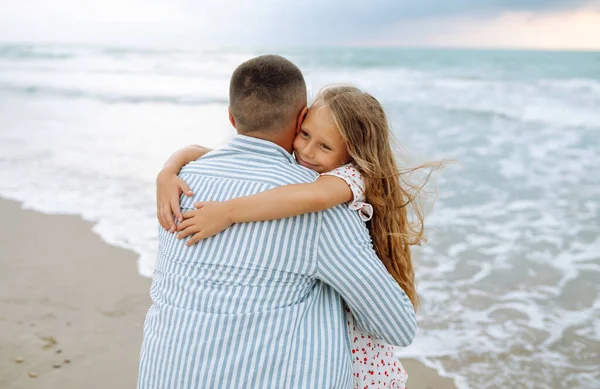 Bir baba ve küçük kızı deniz kıyısında el ele geziyorlar. Mutlu bir adam ve çocuğu dışarıda eğleniyor, birlikte eğleniyorlar. Çocukluk kavramı, rahatlama..