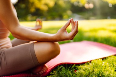 Genç bir kadın güneşli bir parkta yoga minderinde pratik yapıyor. Atletik bir kadın gün batımında dışarıda egzersiz yapar. Rahatlama, dinlenme ve aktif bir yaşam tarzı kavramı.
