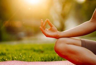 Genç bir kadın güneşli bir parkta yoga minderinde pratik yapıyor. Atletik bir kadın gün batımında dışarıda egzersiz yapar. Rahatlama, dinlenme ve aktif bir yaşam tarzı kavramı.