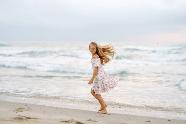 Güzel elbiseli bir kız deniz kıyısında eğleniyor. Kız deniz manzarasını seviyor, deniz kıyısında koşuyor. Çocukluk kavramı, eğlence. Yaşam biçimi.
