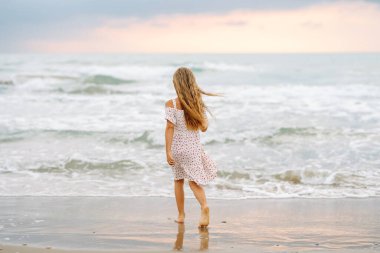 Güzel elbiseli bir kız deniz kıyısında eğleniyor. Kız deniz manzarasını seviyor, deniz kıyısında koşuyor. Çocukluk kavramı, eğlence. Yaşam biçimi.