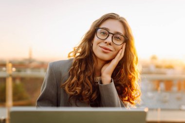 İş kadını, gün batımında bir binanın çatısındaki bir masada dizüstü bilgisayarı üzerinde çalışıyor. Genç bir kadın dizüstü bilgisayarla günbatımının tadını çıkarıyor. İş, serbest meslek kavramı.